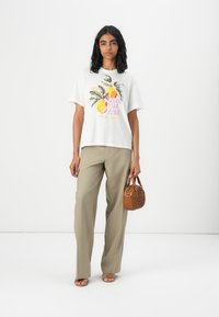Hvid kortærmet t-shirt med frugtgrafik, sammen med lyse khaki-bukser og en lille brun håndtaske, sandaler med flad sål.