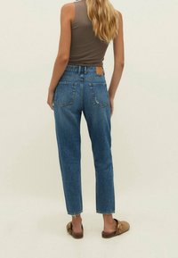 Jeans de mezclilla azul de talle alto con corte recto, costuras visibles, bolsillos traseros y una etiqueta de cuero en la cinturilla.