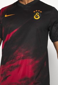 Jersey deportivo negro y rojo con el logo amarillo de Nike y el emblema de Galatasaray que presenta cuatro estrellas y el texto "1905" en el pecho.