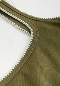 Tank top z ribované látky olivové barvy s bílým cik-cak prošíváním na výstřihu a otvoru na ruce, s plochými švy a hladkou texturou.