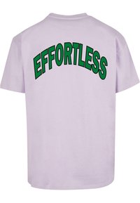 Camiseta de manga corta en color lavanda con gran texto verde que dice "EFFORTLESS" en arco en la parte posterior. Material de algodón suave, corte holgado.