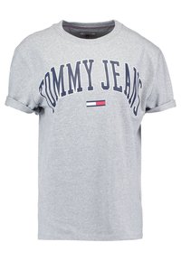T-shirt in cotone grigio con maniche arrotolate, che presenta la scritta "TOMMY JEANS" in testo blu scuro e una piccola grafica della bandiera in rosso, bianco e blu.