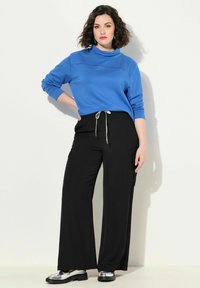 Blauwe pullover met een hoge kraag en gestikte details, gecombineerd met zwarte broeken met wijde pijpen en zilveren schoenen. Eenvoudig, casual ontwerp.