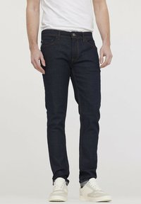 Donkerblauwe denim jeans met een slim fit, voorzien van een traditionele knoopsluiting en zichtbare stikseldetails. Draag ze met witte sneakers.