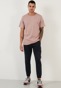 Tricou roz cu mânecă scurtă și decolteu rotund, asociat cu pantaloni joggeri negri. Modelul poartă adidași multicolori, evidențiind un look casual.