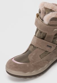 Bottes en daim marron avec des accents roses, des bandes velcro, un doux col en fourrure et une semelle en caoutchouc texturée. Dispose d'un insert imperméable.