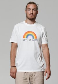 Witte katoenen t-shirt met een kleurrijke regenboogafbeelding en de tekst "LIEFDE IS LIEFDE" eronder. Korte mouwen en ronde hals.