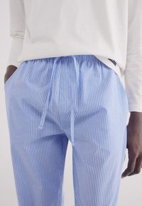 Pantaloni da lounge in cotone azzurro chiaro con strisce verticali bianche, vita elastica e coulisse. Presentano tasche laterali e una vestibilità comoda.