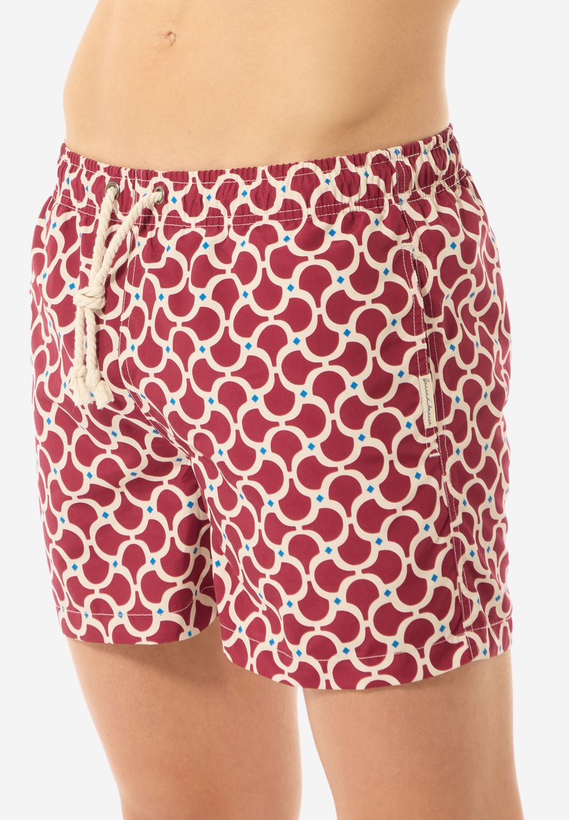 Pantaloni da bagno rossi con un motivo geometrico in crema e dettagli blu. Presentano un elastico in vita con cordoncino e tasche laterali.