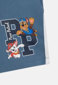 Plava tkanina s likovima iz Paw Patrol-a, smešnim smeškom i crno-belim psom sa tačkama. Dizajn uključuje podebljana slova i jarke boje.