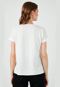 Hvid kortærmet t-shirt med rullekanter, blød bomuldsstruktur, afslappet pasform og rund udskæring, vist fra ryggen.