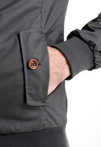 Ciemnoszara kurtka o gładkiej fakturze, z kieszenią zapinaną na guziki i prążkowanymi mankietami. Kieszeń zdobiona jest okrągłym drewnianym guzikiem.