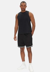Top nero senza maniche abbinato a pantaloni corti in rete neri con accenti bianchi. Il modello indossa scarpe da ginnastica bianche e calze corte.