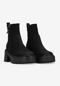 Botas de tobillo de ante negro con cremalleras laterales, suelas de plataforma gruesas y detalles texturizados. Presentan un acabado suave y un diseño robusto.