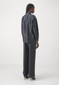 Completo di colore blu scuro, dal fit morbido, realizzato in tessuto strutturato. Camicia a maniche lunghe con colletto, abbinata a pantaloni a gamba larga e scarpe con tacco.