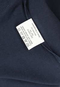 Marinblå bomullstyg med synlig sömnad och tvättråd. Etiketten innehåller tvättanvisningar och produktinformation, sydd på insidan.