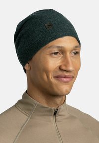 Dark green knit beanie with a textured finish, featuring a small black logo patch. The design is fitted and flexible, suitable for warmth.