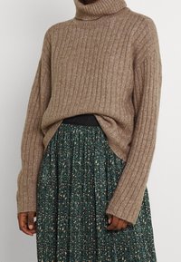 Hnědý žebrovaný rolák spojený se zelenou plisovanou sukní s vysokým pasem a černými a béžovými abstraktními skvrnami.