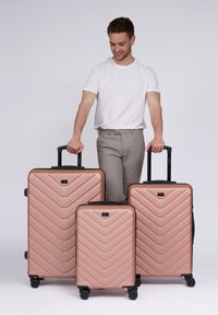 Tres maletas color oro rosa con patrón de espiga, de diferentes tamaños. Hechas de plástico duro con asas y ruedas negras.