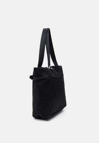 Borsa tote in stoffa nera con lunghe tracolle e dettaglio con fibbia laterale, mostrata su uno sfondo bianco uniforme.