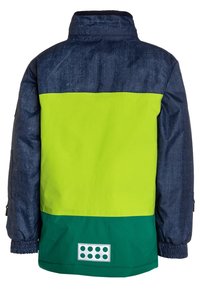 Giacca per bambini con maniche e parte superiore della schiena di colore blu scuro, parte centrale della schiena di colore verde brillante e parte inferiore della schiena di colore verde scuro, con una toppa rettangolare composta da otto punti verdi.