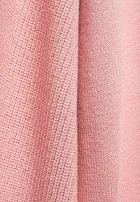 Gros plan sur un tissu tricoté rose plié montrant des motifs de points texturés détaillés et des fibres de fil douces.