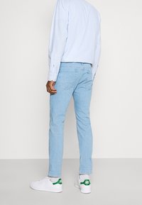 Jeans de mezclilla azul claro con un ajuste slim, bolsillos traseros y costuras en contraste, combinados con zapatillas blancas con detalles en verde.