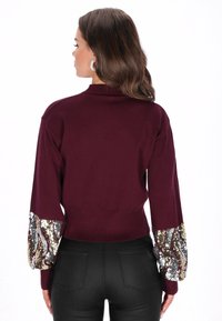Bordeaux sweater met lange, volumineuze mouwen met een sequined patroon. Geribbelde zoom en manchetten, zachte textuur en een getailleerd ontwerp.