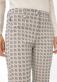 Gemusterte Hose mit einem geometrischen Design in Beigetönen, Schwarz und Grau; aus einem leichten Material mit glatter Textur gefertigt.