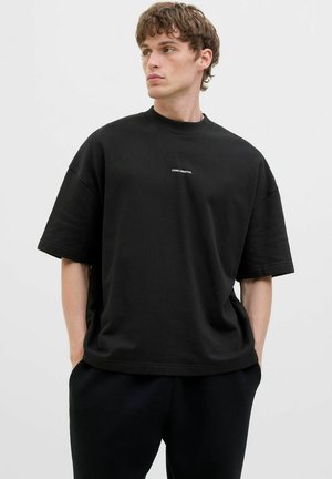 T-shirt noir oversize à manches courtes en coton avec un col rond, présentant un logo blanc "CORE CREATIVE" imprimé sur la poitrine.