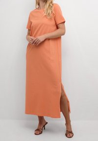 Robe maxi en coton pêche, douce et à manches courtes, avec des fentes latérales pour un mouvement aisément. Elle présente un col rond et une coupe décontractée.