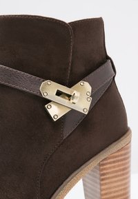 Bruna mockaskinnsankläder med en dekorativ metallspänne och läderrem, med en texturerad brun klack och lager av träådringsmönster.