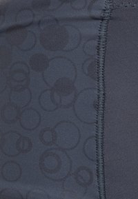 Tissu texturé bleu marine présentant un motif de cercles variés et de sections lisses. Coutures renforcées visibles le long du bord.