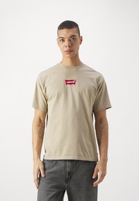 Beige bomulds t-shirt med rund halsudskæring og korte ærmer. Har et rødt broderet Levi's logo på brystet og en afslappet pasform.
