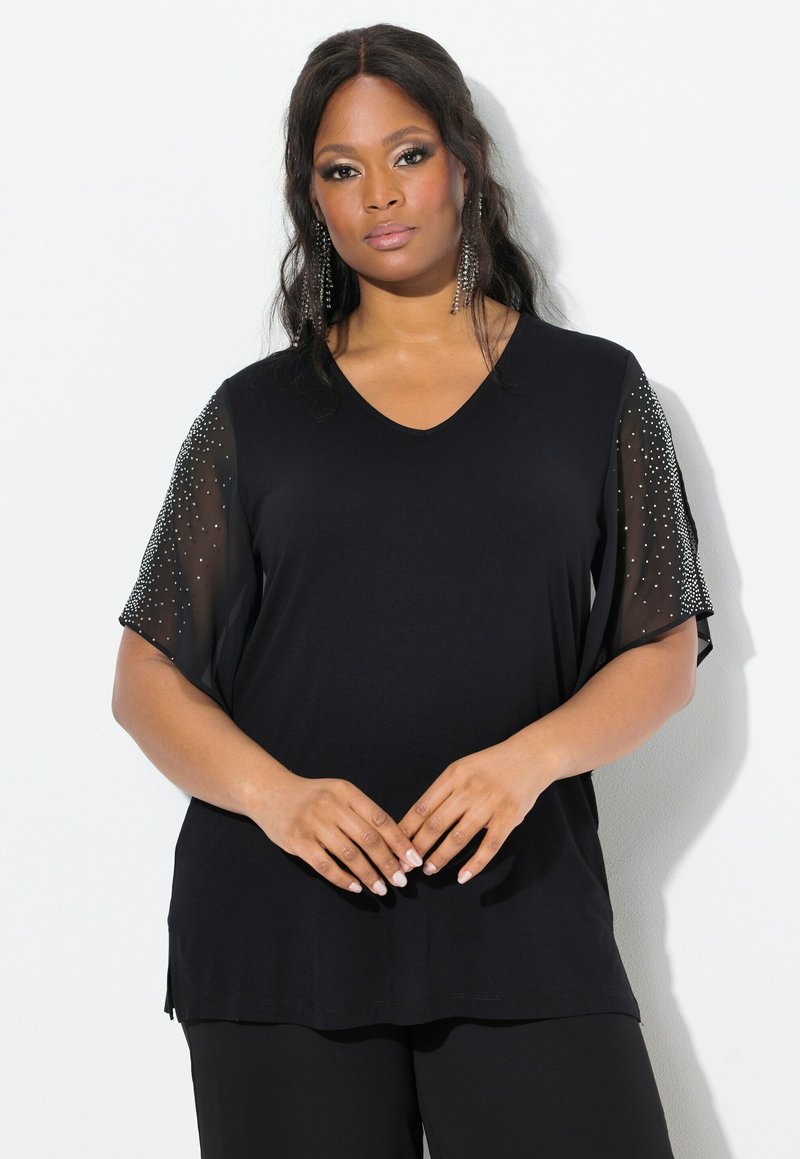 Schwarzes V-Ausschnitt-T-Shirt mit kurzen, transparenten Ärmeln aus Stoff, verziert mit verstreuten Strasssteinen. Weiche Textur, lockere Passform und seitliche Schlitze.