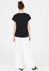 Black short-sleeve shirt paired with white wide-leg pants. The shirt has a round neckline; the outfit features a relaxed fit and lightweight fabric.