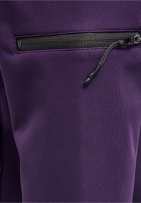 Primo piano di un tessuto viola con una tasca con zip nera dotata di un lembo in tessuto nero su un indumento.