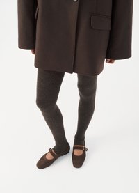 Cappotto in misto lana marrone con grandi bottoni, abbinato a leggings scuri grigi testurizzati e ballerine in suede marroni con cinturino alla caviglia.