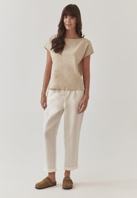 Beige linen top with short sleeves, paired with light beige trousers. Brown slip-on shoes with a flat sole. Simple, relaxed fit.