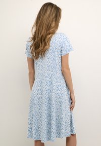Lyhythihainen mekko vaaleansinisestä kankaasta, jossa on valkoinen kukkakuosi, liehukkamallinen design, joka ulottuu polven puoliväliin, sileä rakenne.