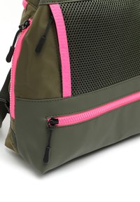 Sac à dos en nylon vert olive avec des accents roses et une poche latérale en mesh. Comprend une poche avant zippée et des détails de couture contrastés.