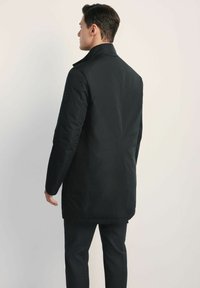 Czarna izolowana kurtka z długim dołem, wysokim kołnierzem i teksturowanym materiałem. Posiada logo na ramieniu i dopasowany krój.