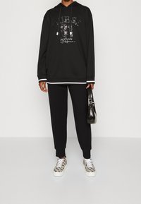 Sudadera negra con gráficos de lentejuelas, combinada con pantalones de chándal negros. Zapatillas texturizadas con un diseño de estampado de leopardo. Acentuada con un pequeño bolso negro.