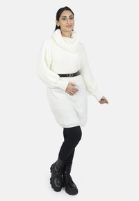 Witte, geribbelde, oversized trui met een col, gecombineerd met zwarte legging en chunky zwarte veterlaarzen. Geaccentueerd met een zwarte riem met een hartvormige gesp.