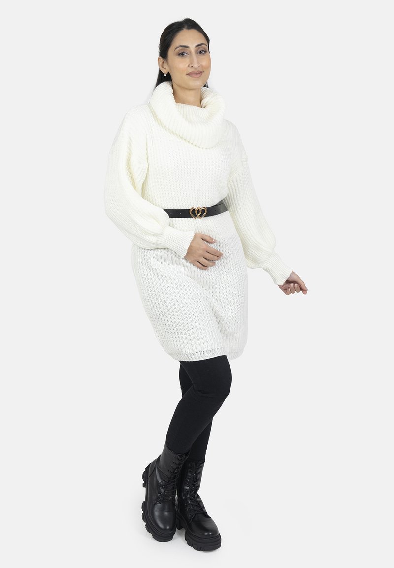 Hvid strikket sweaterkjole med en cowl-udskæring og lange ærmer, parret med et sort bælte med en hjerteformet spænde, sorte leggings og støvler.