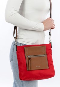 Červená nylonová crossbody taška s přední kapsou z hnědé kůže, stříbrným zipem a nastavitelným popruhem. Disponuje texturovaným povrchem.
