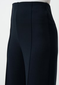 Pantalons taille haute bleu marine en tissu doux, avec une coupe droite, des lignes épurées et des détails de couture avant pour plus de structure.