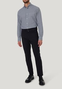 Schwarze schmal geschnittene Hose mit Knopfverschluss, kombiniert mit einem blau-weißen karierten Langarmhemd und schwarzen Schnürschuhen.