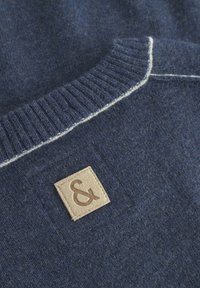 Marineblauer Strickpullover mit einem gerippten Kragen und heller Kontrastnaht, versehen mit einem beigen strukturierten Etikett mit einem kaufmännischen Und-Zeichen.