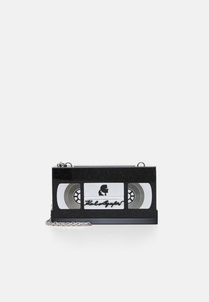 Sac à main rectangulaire noir en forme de cassette VHS avec une bandoulière chaîne argentée et un petit logo silhouette sur le devant.